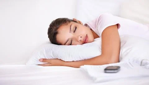 Taking some time out. A young woman sleeping on her bed with her phone and work Stock Photos
