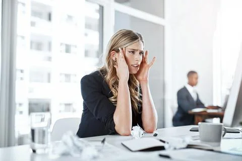 Taking work stress to the head. a young businesswoman experiencing stress while Stock Photos