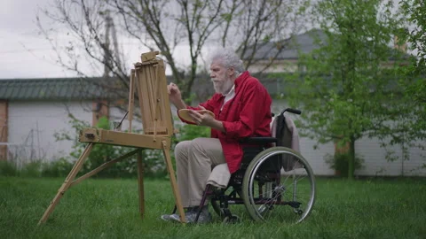 Talented creative disabled old man painting on easel in spring summer garden on 스톡 동영상 158334208