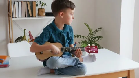 Talented kid playing soprano ukulele sitting on desk Stock Footage 150732653