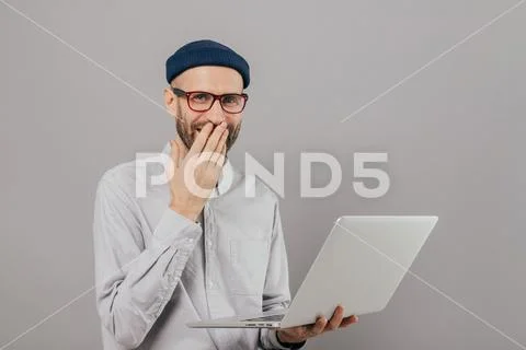 Talented male graphic designer works remotely on gadget, laughs positively, c Stock Photos