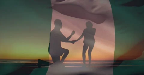 Talking couple stepping closer, kneeling man proposing on beach sunset with flag Stock Footage 331565674