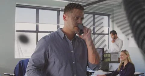 Talking foreground man wearing button-down shirt holding smartphone near blinds Stock Photos