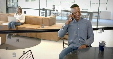 Talking man wearing button-down shirt and jeans smiling on smartphone at office Stock Photos