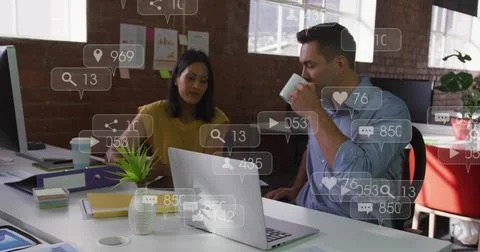 Talking pair leaning over open laptop in office mustard top blue shirt coffee Fotos Stock