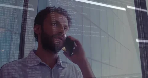 Talking on phone, man with computer code overlaying glass office wall Stock Footage 328083992