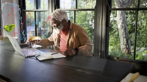 Talking senior man in rust top at workspace, holding phone, writing notebook at Stock Footage 332468081