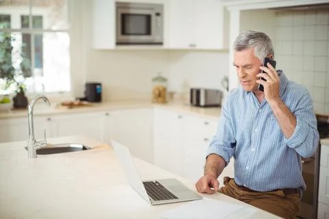 Talking senior man using smartphone and checking laptop with papers at marble Stock Photos