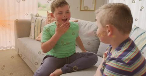 Talking two boys sitting on gray sofa in living room with patterned pillows, Stock Photos