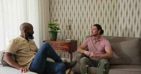 Talking two men sitting on sofa and armchair in living room, wearing shirts, Stock Photos