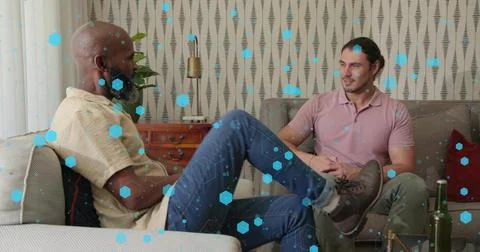 Talking two men sitting on sofas in living room, noting green bottle and blue Stock Photos