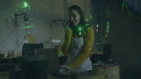 Talking white-aproned mustard-top woman typing on laptop, phone at wood bench Stock Footage 333609631