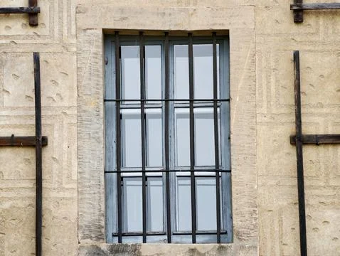 Tall barred window in textured stone wall with metal supports Stock Photos