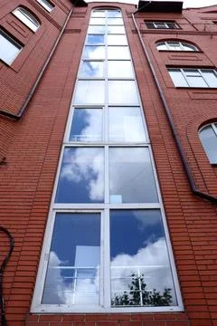 Tall brick building with large windows reflecting clouds in the sky Foto stock
