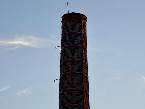 Tall brick chimney stack silhouetted against pale evening sky, warm sunligh.. Stock Photos