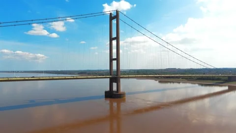 Tall bridge spans muddy river under bright blue sky Vidéo 343545643