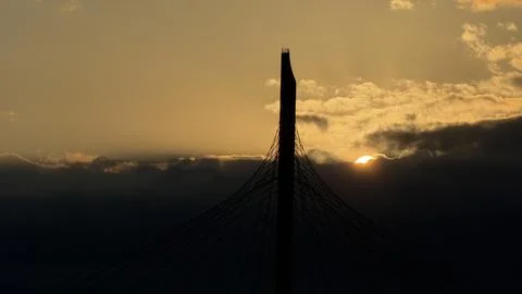 Tall cable-stayed bridge pylon in dark silhouette against a moody sunset sky Stock Photos