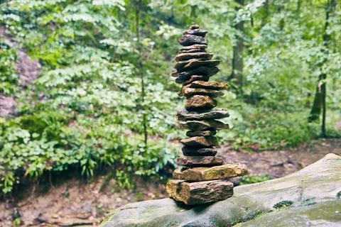 Tall cairn stack of stones on muted green forest background Stock Photos