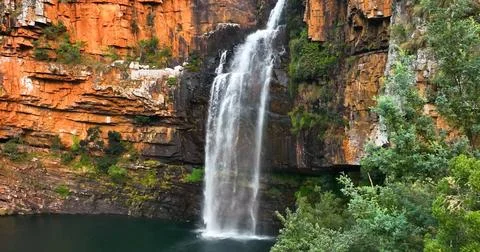 A tall, cascading waterfall flows over a rocky cliff into a deep pool. Stock-Fotos