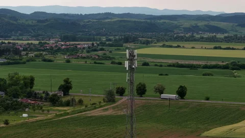 A tall cell tower stands prominently within a vast, green rural landscape Stock Footage 338377237