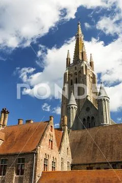 Tall church steeple of the Church of our Lady in medieval city of Bruges with bl Stock Photos