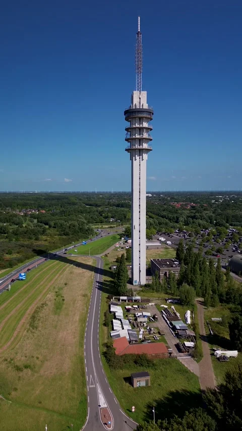 A tall communication tower rises above green landscapes and winding roads Vídeos de archivo 315338422