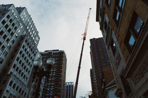 A tall construction crane is positioned between several buildings in a city.  Stock Photos