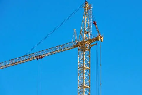 A tall construction crane is seen working under a clear blue sky Stock Photos