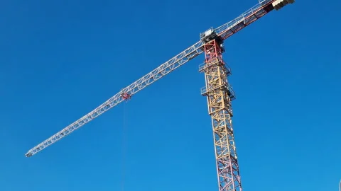 Tall construction tower crane rotating its jib arm against a clear blue sky.  Stock Footage 327158995