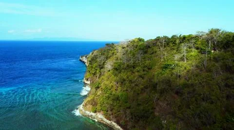 The tall elephant cliffs blocking the waves are covered with green trees and  Stock Photos