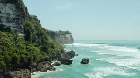 The tall elephant cliffs blocking the waves are covered with green trees and  Stock Photos