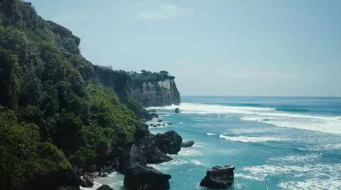 The tall elephant cliffs blocking the waves are covered with green trees and  Stock Photos