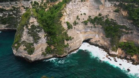 The tall elephant cliffs blocking the waves are covered with green trees and  Stock Photos