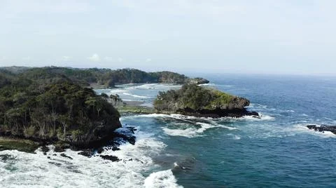 The tall elephant cliffs blocking the waves are covered with green trees and  Stock Photos