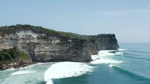 The tall elephant cliffs blocking the waves are covered with green trees and  Stock Photos