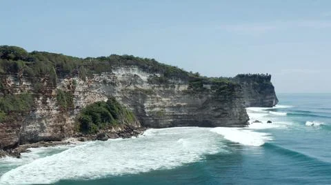The tall elephant cliffs blocking the waves are covered with green trees and  Stock Photos