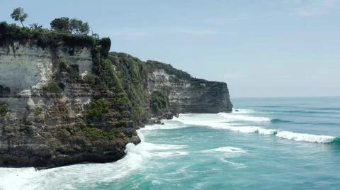 The tall elephant cliffs blocking the waves are covered with green trees and  Stock Photos