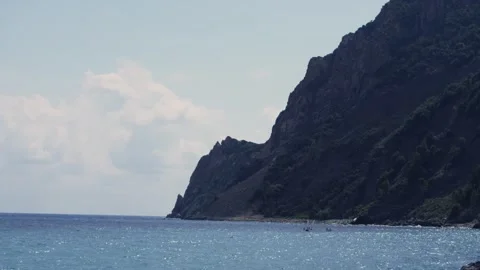 Tall Forested Cliff Rising Above Open Sea, Distant Sailboats, Panoramic Shot Stock Footage 340631085
