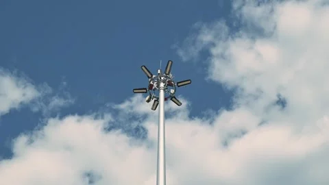A tall light pole stands against a blue sky filled with scattered clouds. This Stockbeeldmateriaal 344525818