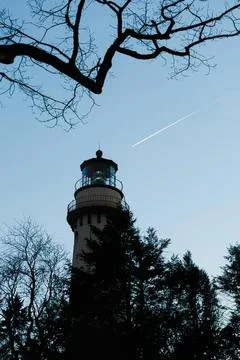 Tall lighthouse with leafless tree branches against blue sky Stock Photos
