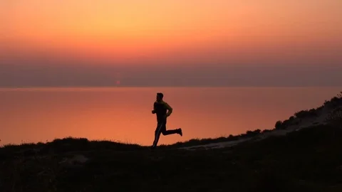 Tall man is running on the beach at sunset. Silhouette of sport active man Stock Footage 124428648