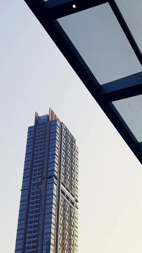 Tall modern skyscraper rises beside a geometric steel canopy against a pale.. Stock Footage 340115985