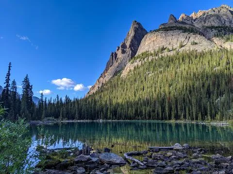 A tall mountain covered in pine trees reflects off a small turquoise lake Stock Photos