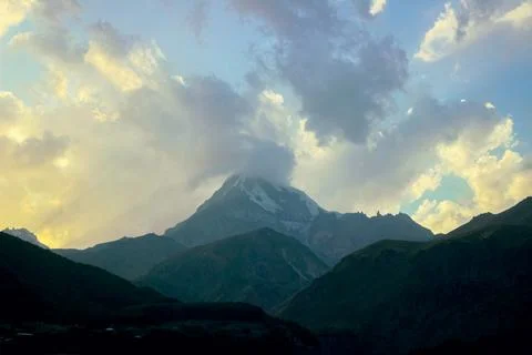 Tall mountain peaks beneath dramatic clouds illuminated by soft evening light Stock Photos