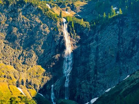 Tall Mountain Waterfall Cascading Down Rocky Cliff Surrounded by Alpine Mea.. Stock Photos