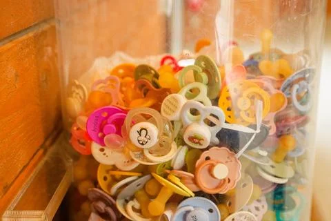 Tall plastic container filled with colorful baby pacifiers Stock Photos