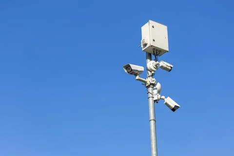 A tall pole with three security cameras and a box against a clear blue sky Stock Photos