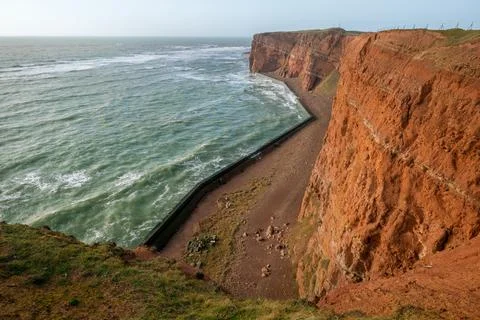 Tall red dramatic cliffs of Heligoland island with rough sea. Sunny windy winter Stock Photos
