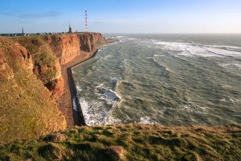Tall red dramatic cliffs of Heligoland island with rough sea and a lighthouse Stock Photos