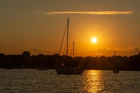 Tall sailboat without sails at sunset with a bright orange sky Stock Photos
